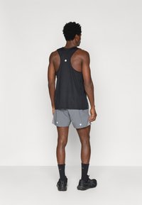 Μαύρη αμάνικη αθλητική μπλούζα με υφή, συνδυασμένη με γκρι σορτσάκια. Και τα δύο διαθέτουν λευκές στρογγυλές λεπτομέρειες. Συμπεριλαμβάνονται αθλητικά παπούτσια και κάλτσες.