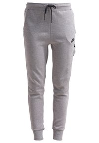 Pantalon de jogging Nike gris clair avec cordon noir, jambes fuselées, poignets élastiques, poche latérale zippée et logo Nike sur la cuisse.