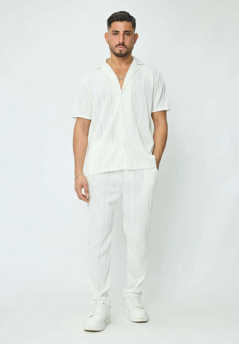 Chemise blanche et pantalon assorti avec un motif de vague texturé, fabriqués dans un tissu léger. La tenue est associée à des baskets blanches.