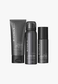 Trzy produkty pielęgnacyjne Rituals Homme: peeling do twarzy z węglem w szarym tubie, szara butelka pianki pod prysznic oraz czarny dezodorant w sprayu.