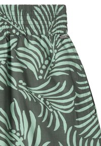 Gros plan sur un short vert foncé avec un motif de feuilles tropicales vert clair et une ceinture élastique.