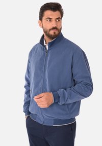Giacca bomber blu realizzata in tessuto liscio. Presenta un colletto rialzato, chiusura con zip frontale e polsini a coste. Design semplice senza motivi visibili.
