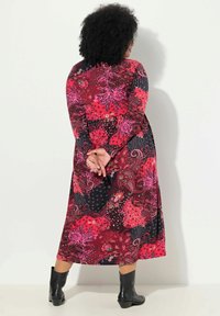 Pitkä, monivärinen mekko punaisilla, vaaleanpunaisilla sekä mustilla kukkakuosisilla ja paisley-kuosisilla. Mekossa on pitkät hihat ja liehuva siluetti, jota on täydentämässä mustat nilkkurit.