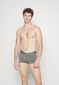 Boxer da uomo grigi in cotone con una morbida fascia elastica decorata con il logo Calvin Klein, indossati da un modello con capelli corti e ricci.
