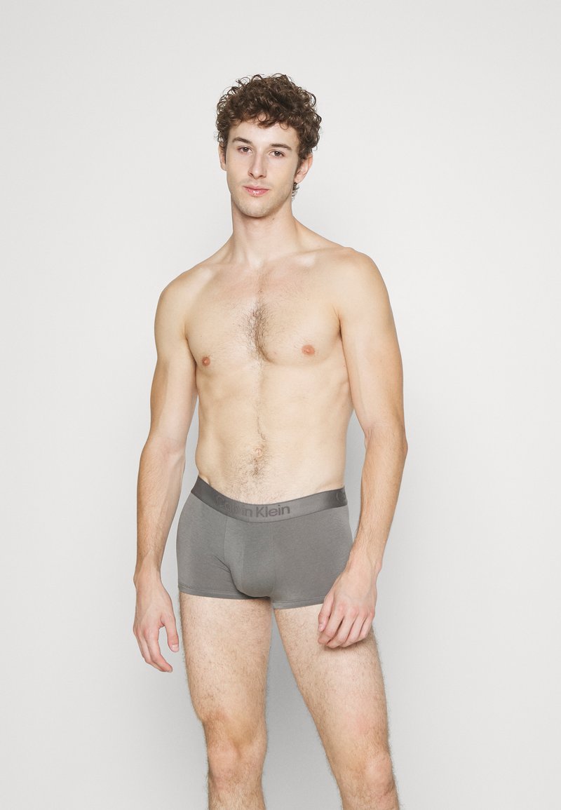 Boxer da uomo grigi in cotone con una morbida fascia elastica decorata con il logo Calvin Klein, indossati da un modello con capelli corti e ricci.