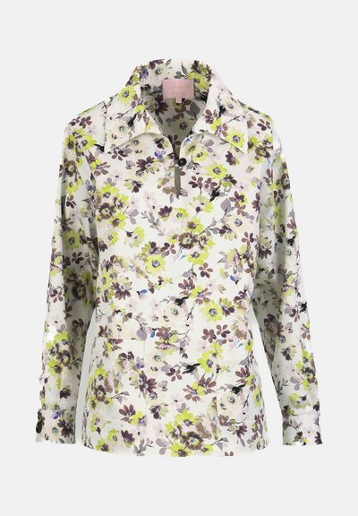 Blouse blanche à manches longues avec imprimé floral vert, marron et violet, col boutonné et deux poches plaquées avant.