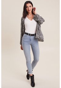 Blazer à motifs noir et blanc porté sur un t-shirt blanc à col en V, associé à un jean skinny bleu clair et des bottines noires à talons. Collier en chaîne argenté inclus.