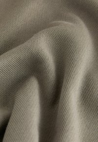 Gros plan sur un tissu beige texturé avec un motif de tricot visible et des plis doux et fluides.