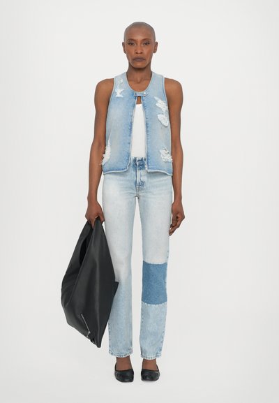 Džinsvest, millel on kulunud detailid, koos helesiniste lapitekkide teksadega. Modelle hoiab musta nahkkinga, jalas on mustad lamedad kingad.