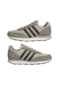 Une paire de baskets beige et grises avec des rayures noires, des semelles intermédiaires blanches et des semelles extérieures noires, présentée en vue latérale sur fond blanc.