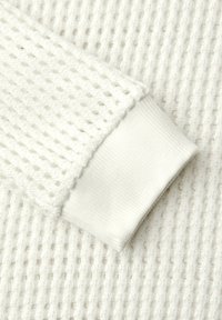 Tissu en nid d'abeille blanc avec bord-côte blanc côtelé, mettant en valeur le contraste de texture et le détail de la manche.