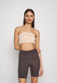 Beige strapless topp med ruchad mittendel, kombinerad med mörkbruna, tighta cykelbyxor. Slät textur, sömlös design och minimalistisk stil.