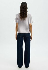 Stripet t-skjorte med korte ermer, kombinert med vidde mørkeblå jeans. T-skjorten har horisontale striper i lyse og mørke farger.