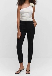 Haut blanc à une épaule avec une texture froncée et un accent floral, associé à un pantalon noir ajusté et des sandales à talons noires.