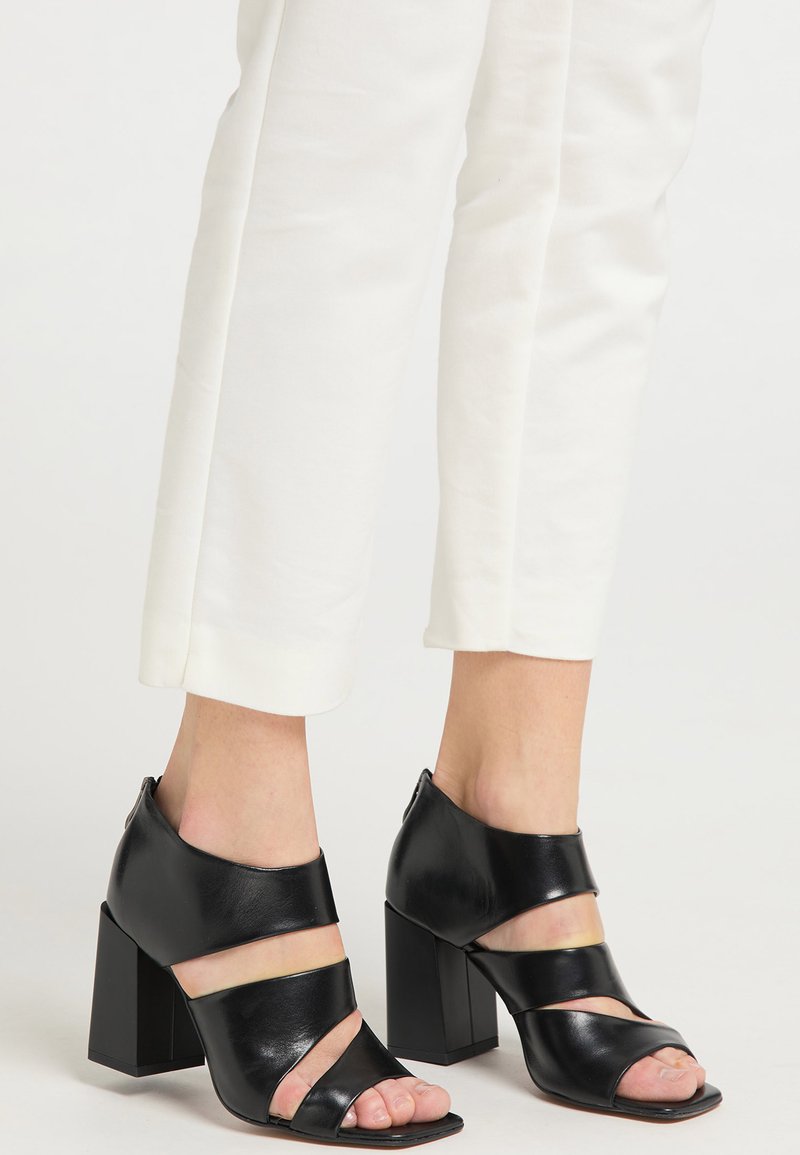Schwarze Leder-High-Heel-Sandalen mit offenem Zeh, ausgestattet mit breiten Riemen und einem klobigen, quadratischen Absatz. Glatte Textur und minimalistisches Design.