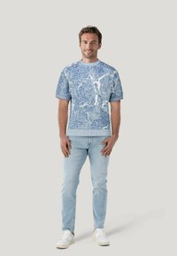 Maglione a maglia azzurro chiaro con motivi, maniche corte, scollo rotondo e dettagli testurizzati, abbinato a jeans azzurri chiari e sneakers bianche.
