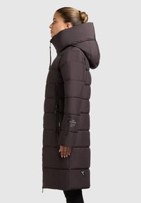 Donsjack in donkerbruin, met een hoge kraag, ritszakken, gequilt ontwerp en een slanke silhouet. Zwarte accenten op de mouwen.