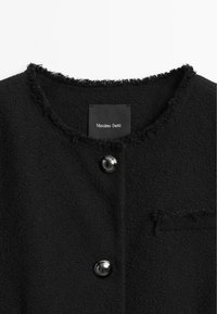 Svart ullblandad jacka med en fransig halsringning, som har en enda bröstficka och två glansiga knappar. Lappen läser "Massimo Dutti."