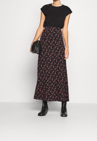 Zwart topje met korte mouwen, gecombineerd met een lange, bloemige rok met rode en roze accenten op een zwarte achtergrond. Zwarte enkellaarsjes en een clutch.