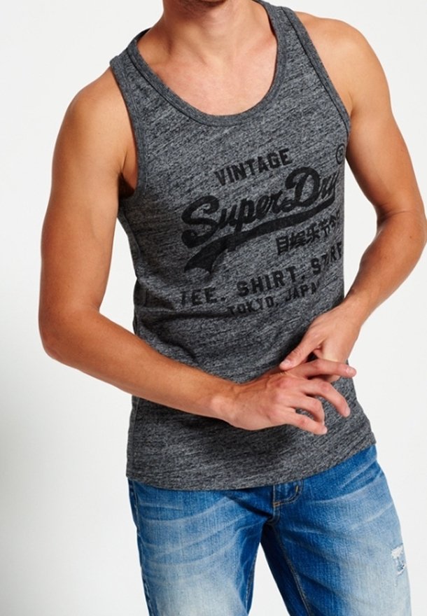 Camiseta sin mangas gris con texto negro "SuperDry", cuello redondo y diseño sin mangas. Combinada con unos vaqueros azul claro, ligeramente desgastados.