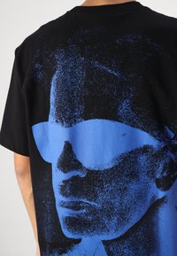Black cotton t-shirt featuring a large blue graphic of a face with sunglasses on the back, textured print with a slightly grainy finish.