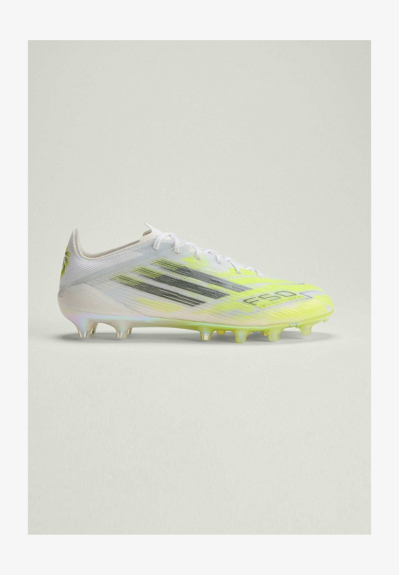 Λευκό και νέον κίτρινο ποδοσφαιρικό παπούτσι με μαύρες ρίγες και διαμορφωμένες τάπες σε απλό ανοιχτό φόντο, φαίνεται από το πλάι.