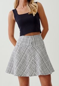 Top corto nero abbinato a una gonna plissettata a vita alta, lunga fino al ginocchio, con un motivo a scacchi bianco e nero.