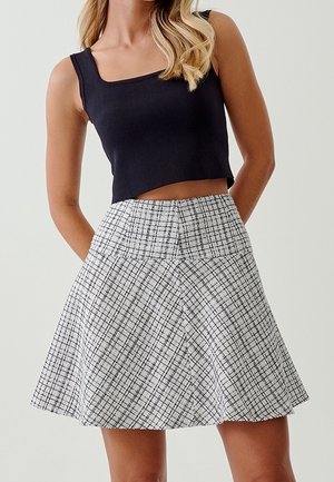 Top court noir sans manches associé à une jupe plissée taille haute, longueur genou, arborant un motif à carreaux noir et blanc.