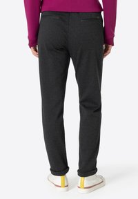 Dark, textured trousers with a slim fit, featuring a rolled hem. Worn with white sneakers accented with yellow details.