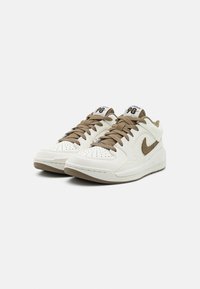 Bílé a hnědé tenisky s hladkým koženým svrchním dílem, perforovanou špičkou, plochými tkaničkami a polstrovanou podrážkou s hrubou hnědou podrážkou.