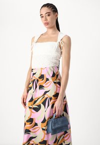 Vit smockad crop top med band; färgglad, mönstrad maxi kjol i rosa, orange och svart; blå mockaväska med handtag.