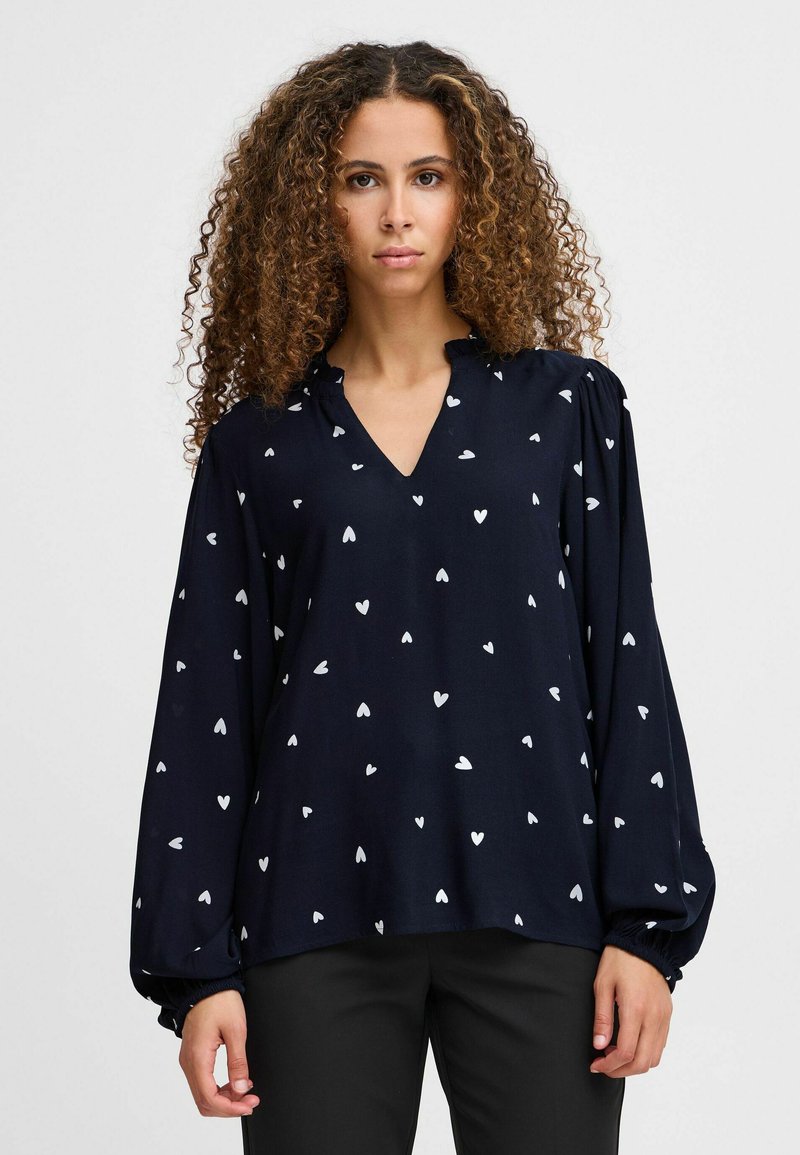 Marineblouse met een V-hals, lange pofmouwen en witte hartpatronen overal. Zachte stof zorgt voor een soepele textuur.