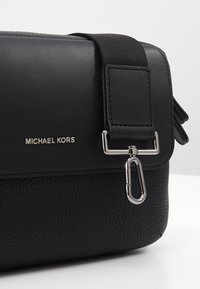 Borsa a tracolla in pelle nera con finitura testurizzata, hardware argentato e logo brandizzato. Presenta una tracolla rimovibile e dettaglio con chiusura.