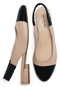 Chaussures slingback en cuir beige avec un bout noir, un talon bloc sculpté et un détail de sangle noire tressée. Texture lisse, design épuré.
