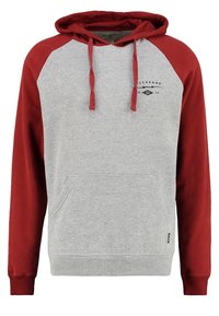 Sudadera gris con mangas raglán rojas. Presenta un bolsillo frontal, capucha con cordón y un pequeño detalle de logo en el pecho. Textura de tela suave.