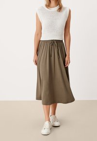 Top senza maniche bianco a maglia con orlo a coste abbinato a una gonna maxi verde oliva scuro con coulisse, indossato con sneakers bianche.