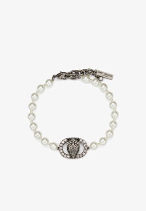 Armband met een rij witte parels, een centrale ovale zilveren sluiting versierd met kristallen, en een metalen kettinkje met de gravure "Kurt Geiger London".