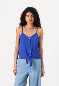 Royal blue, teksturert tank topp med tynne stropper, v-hals og en front knute detalj. Har en knappliste med runde knapper.