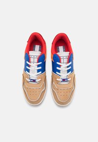 Zapatillas multicolores con una base de gamuza color canela, superposiciones sintéticas en azul y rojo, acentos blancos, detalles perforados y cordones en contraste.