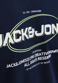 Marineblå bomulds t-shirt med hvid og lysegrøn tekst. Designet inkluderer brandlogo, etableringsår og stedoplysninger.
