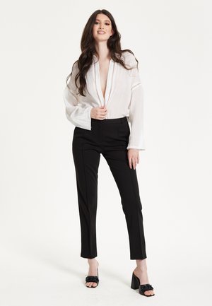 White linen blouse with deep V-neck and lace detailing, paired with high-waisted black trousers and black mules with a textured strap.