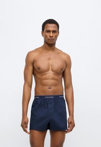 Μπλε ναυτικό μαγιό σορτς από ελαφρύ ύφασμα με ελαστική μέση που φέρει λευκό λογότυπο Calvin Klein. Ομαλή υφή και κλασική κοπή.
