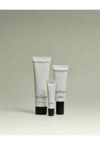 Trois tubes de soins de la peau : un gel douche corporel blanc, une crème pour les mains blanche nourrissante et un petit baume à lèvres, tous avec un design minimaliste et un texte noir.