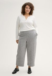 Top blanco de manga larga con escote tipo henley, combinado con pantalones de pierna ancha en patrón de espiga gris y zapatos negros.
