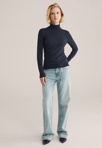 Jūras spēku turtlenecks džemperis mīkstā audumā, kombinēts ar gaiši zilo platā kāju biksēm un melniem smailiem apaviem. Vienkāršs un piegulošs dizains.