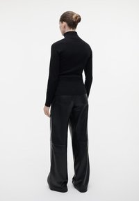 Schwarzes Turtleneck-Oberteil kombiniert mit locker sitzenden schwarzen Lederhosen. Glatter Stoff mit strukturierten Details am Oberteil und an den Hosen.