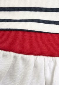 Maglietta a righe con strisce orizzontali bianche e blu navy, una vita a coste rossa e un orlo arricciato bianco per texture e contrasto visivo.