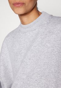 Sudadera gris con cuello redondo acanalado. Textura suave, ajuste relajado y detalle de costura visible. No presenta patrones ni acentos.