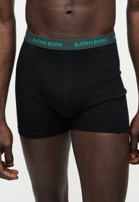 Αντρικός κορμός που φοράει μαύρα μποξέρ με σκούρα πράσινη ζώνη μέσης με την επιγραφή "BJÖRN BORG" σε τυρκουάζ χρώμα.