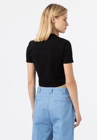 Black cropped t-shirt with short sleeves, paired with light blue tailored trousers featuring back pockets and a small logo.